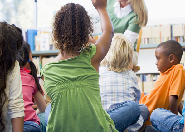 Kindergarten teacher reading to children in library, girl lookin
